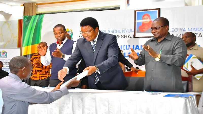 Waziri Mkuu, Kassim Majaliwa, akikabidhi cheti cha kijiji kwa mmoja wa viongozi wa vijiji wakati wa mkutano wa wadau kuhusu utekelezaji Mradi wa Uboreshaji Usalama wa Milki za Ardhi, uliofanyika Ruangwa mkoa wa Lindi. 