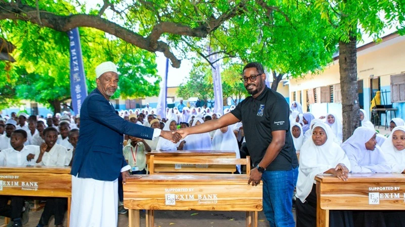 The District Commissioner for South Unguja, Hon. Othman Ali Maulid (left), receives one of 80 school desks from the Head of Marketing and Communications at Exim Bank Tanzania, Stanley Kafu (right) as a symbolic gesture of the bank's commitment to giving